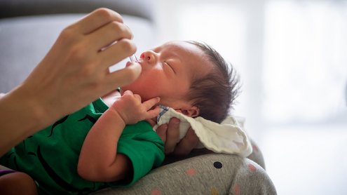 S&auml;ugling wird gehalten und Vitamintropfen in seinen Mund getr&ouml;pfelt.